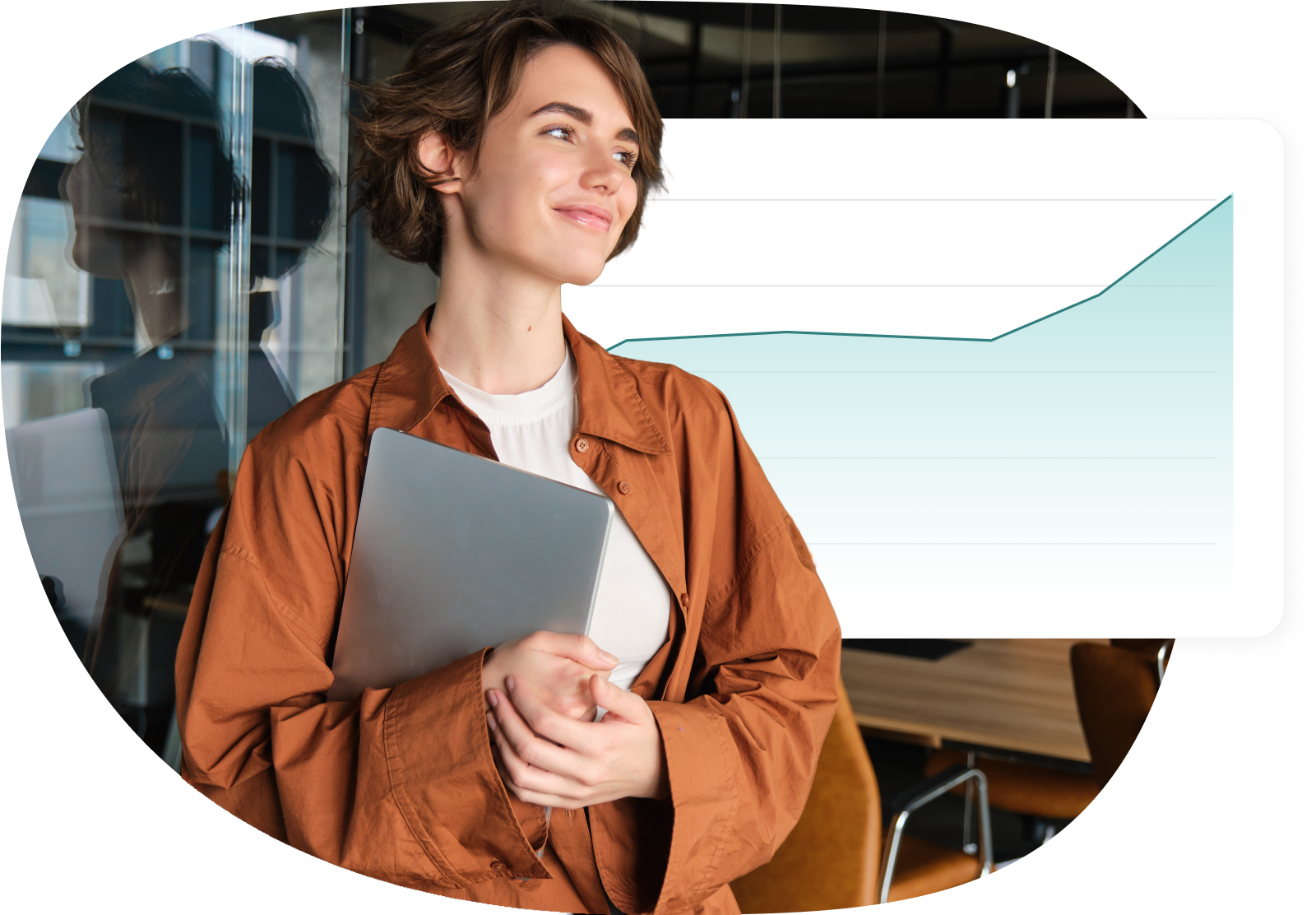  Confident woman holding a laptop, standing in front of a rising graph in a modern office setting.